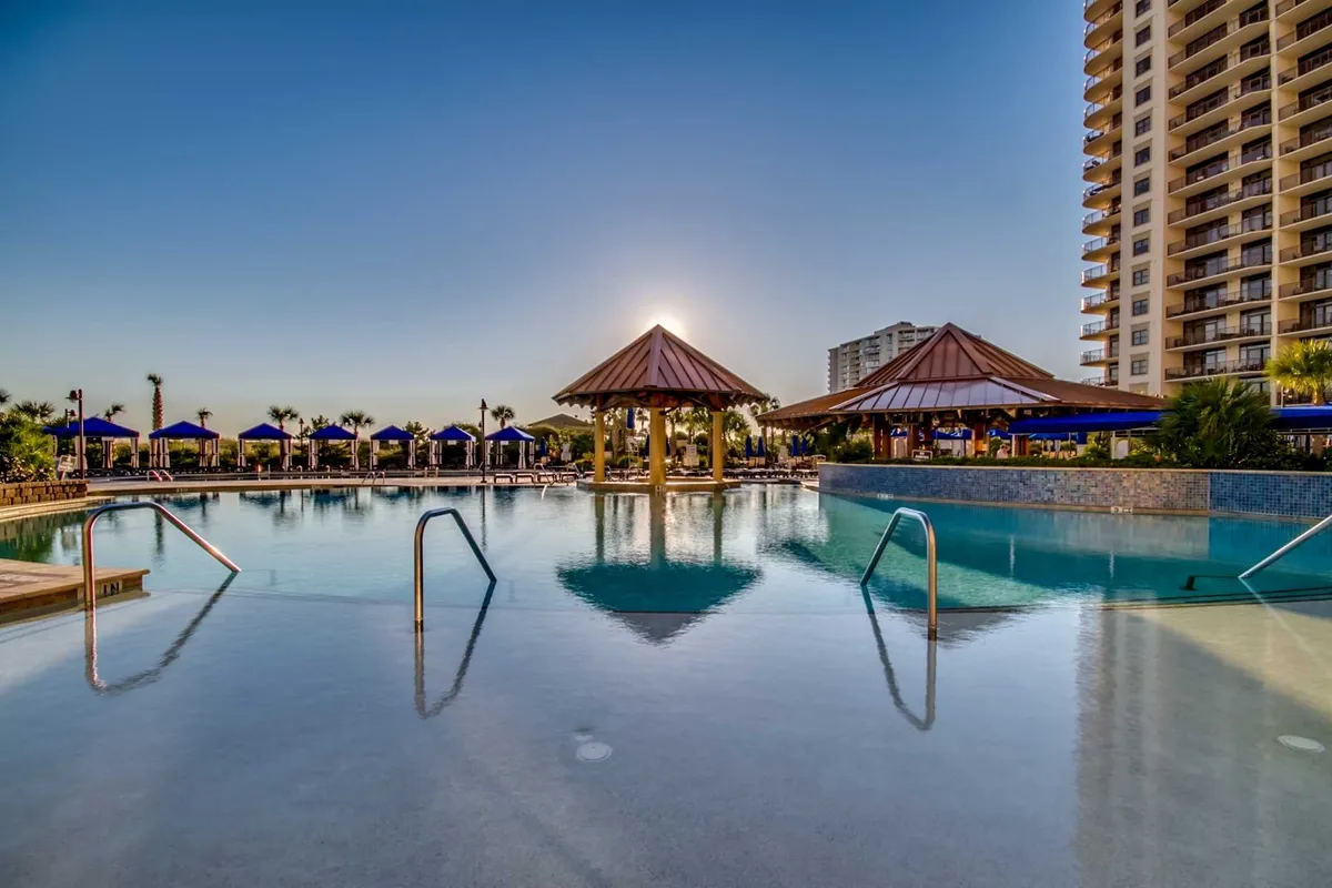 A tranquil pool scene featuring thatched-roof cabanas, abundant lounge seating, and swaying palm trees. The area exudes a peaceful, exclusive vibe—ideal for both family fun and quiet relaxation.
