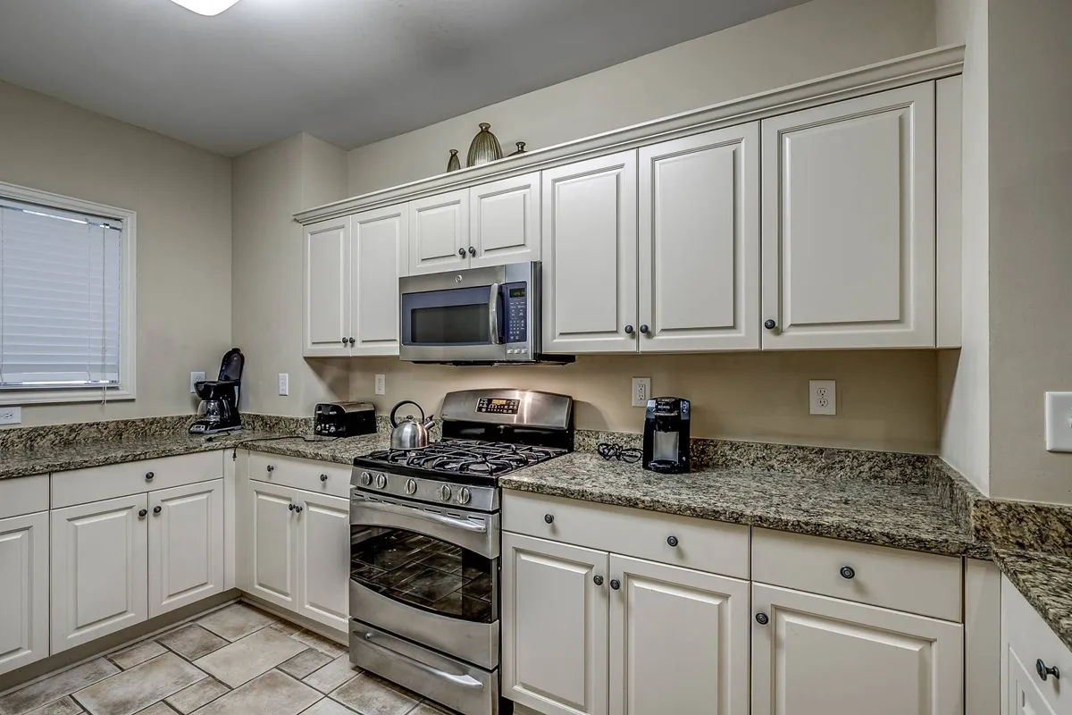 This image showcases a welcoming kitchen space featuring gleaming stainless steel appliances, granite countertops, and ample cabinetry. The room is designed for group cooking and social gatherings, with plenty of workspace and a layout that encourages shared activity. The scene captures the inviting atmosphere where families or friends can cook together, celebrate holidays, and share recipes.