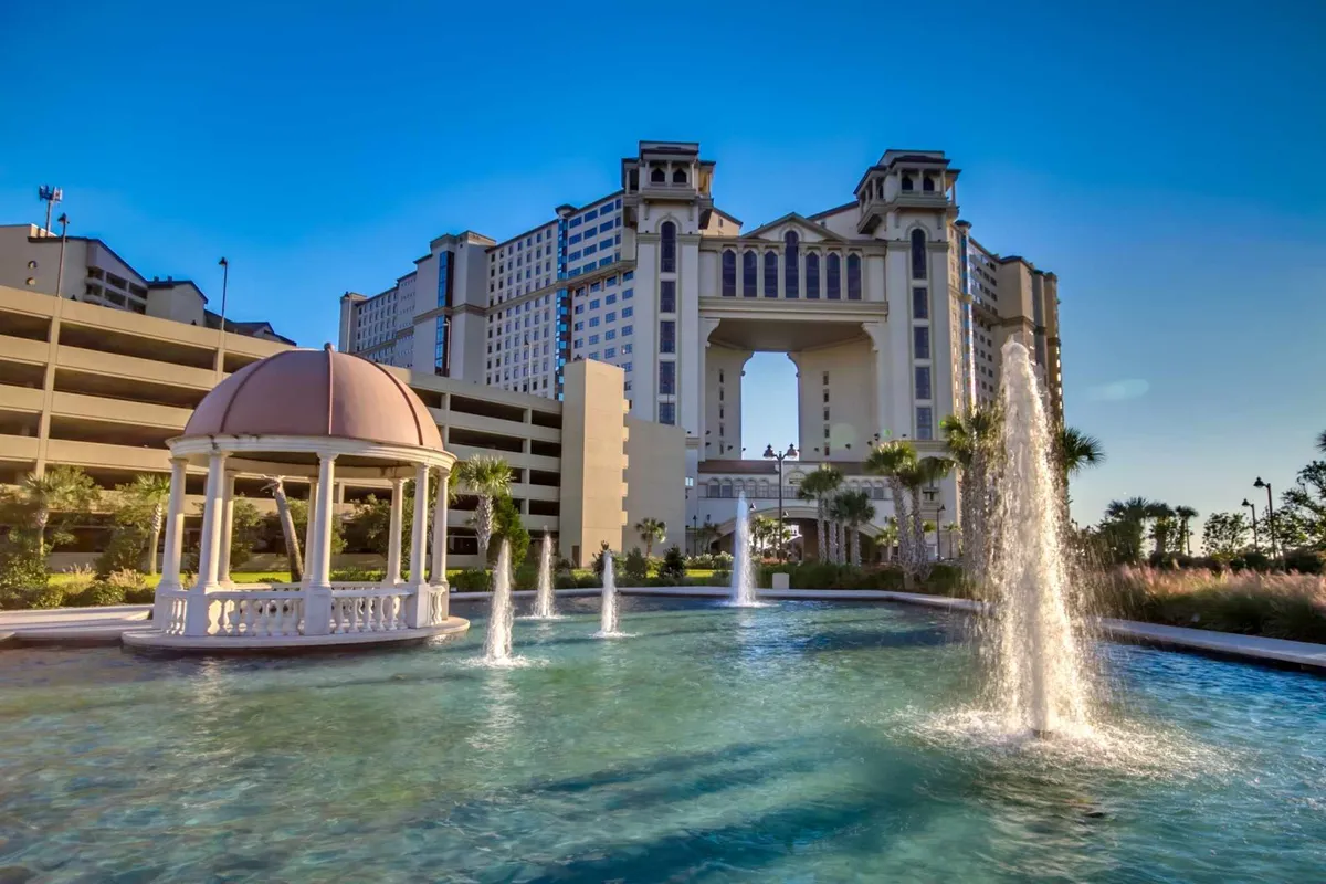 An elegant gazebo sits beside a decorative water fountain, surrounded by manicured gardens and lush landscaping. The scene is tranquil and inviting, with soft lighting suggesting the transition from day to evening. The setting hints at the kind of serene, upscale environment perfect for unwinding after an active day.